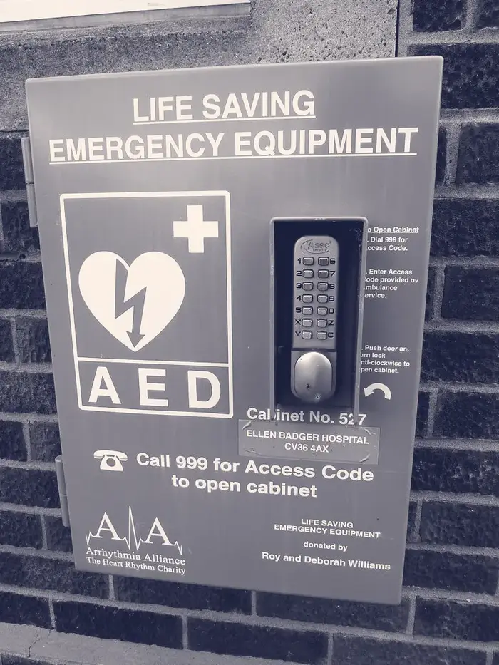 A green public defibrillator cabinet on a brick wall with a keypad and the sign: call 999 for access code